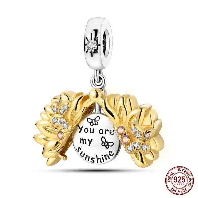 A sterling silver charm featuring a golden sunflower with green leaves on a heart-shaped base.