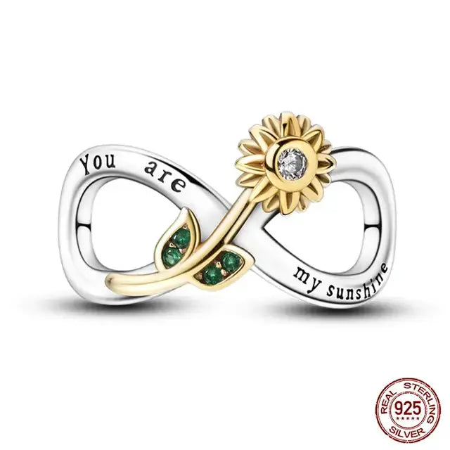 A sterling silver charm featuring a golden sunflower with green leaves on a heart-shaped base.