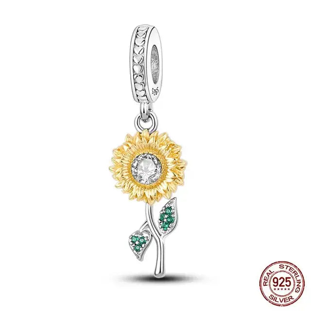 A sterling silver charm featuring a golden sunflower with green leaves on a heart-shaped base.