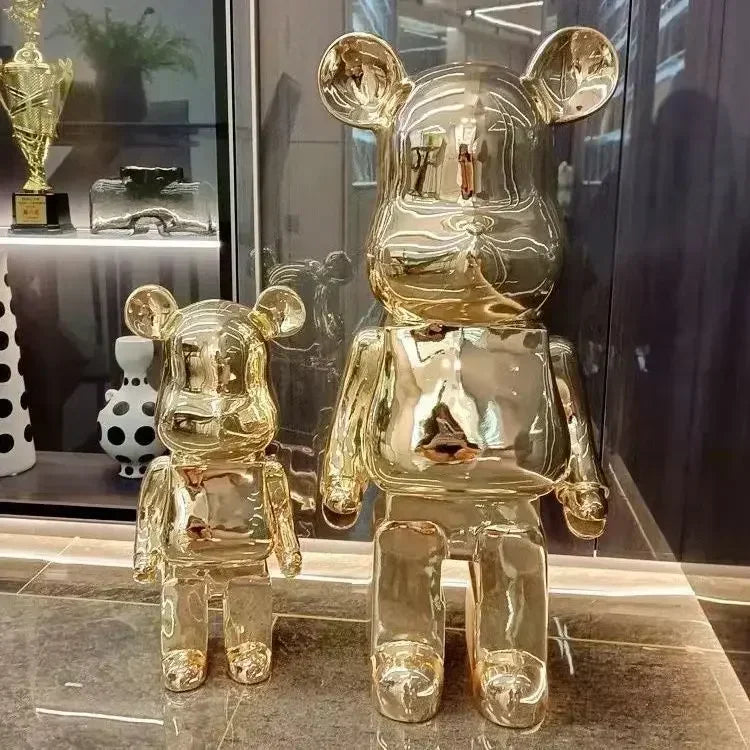 Two gold bear-like figurines on a reflective surface with a blurred background bearbrick collectable