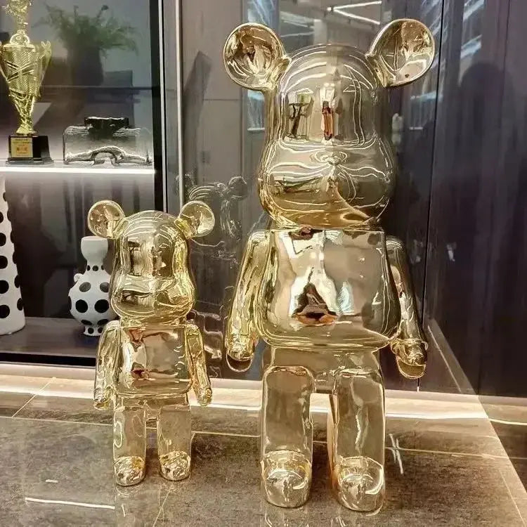 Two gold bear-like figurines on a reflective surface with a blurred background bearbrick collectable