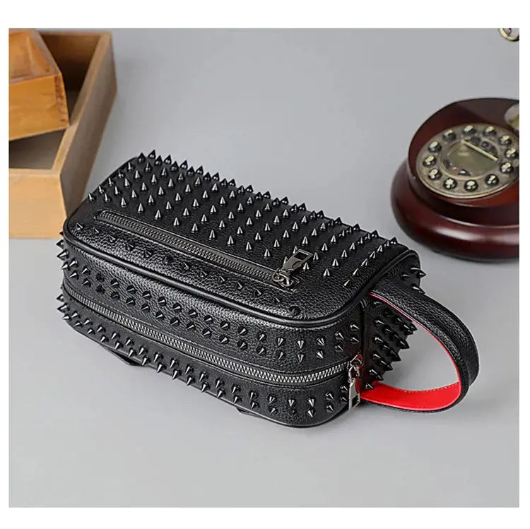 Black studded handbag with a red strap on a gray surface