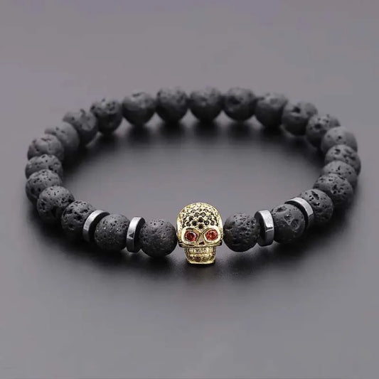 Black beaded bracelet with a gold skull charm on a gray background