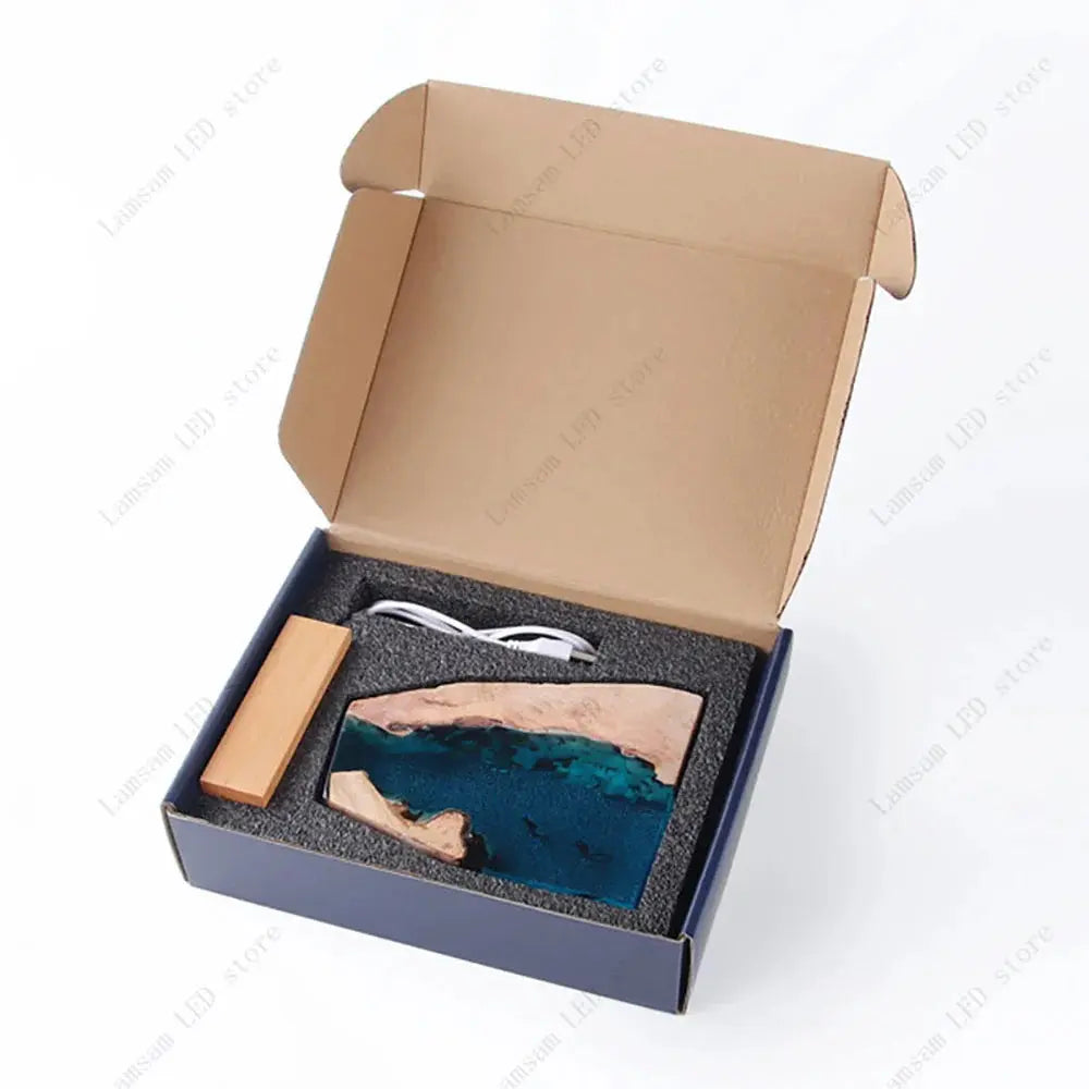Open box containing a decorative item with a wooden base and blue resin design, on a white background.