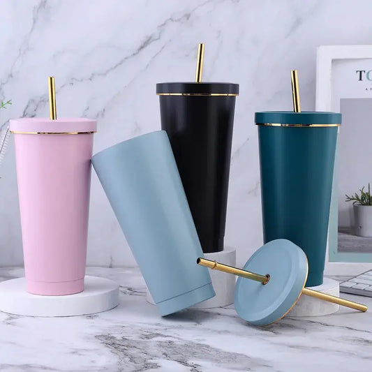 Set of four insulated tumblers in pink, blue, black, and green with gold lids and straws on a marble surface.