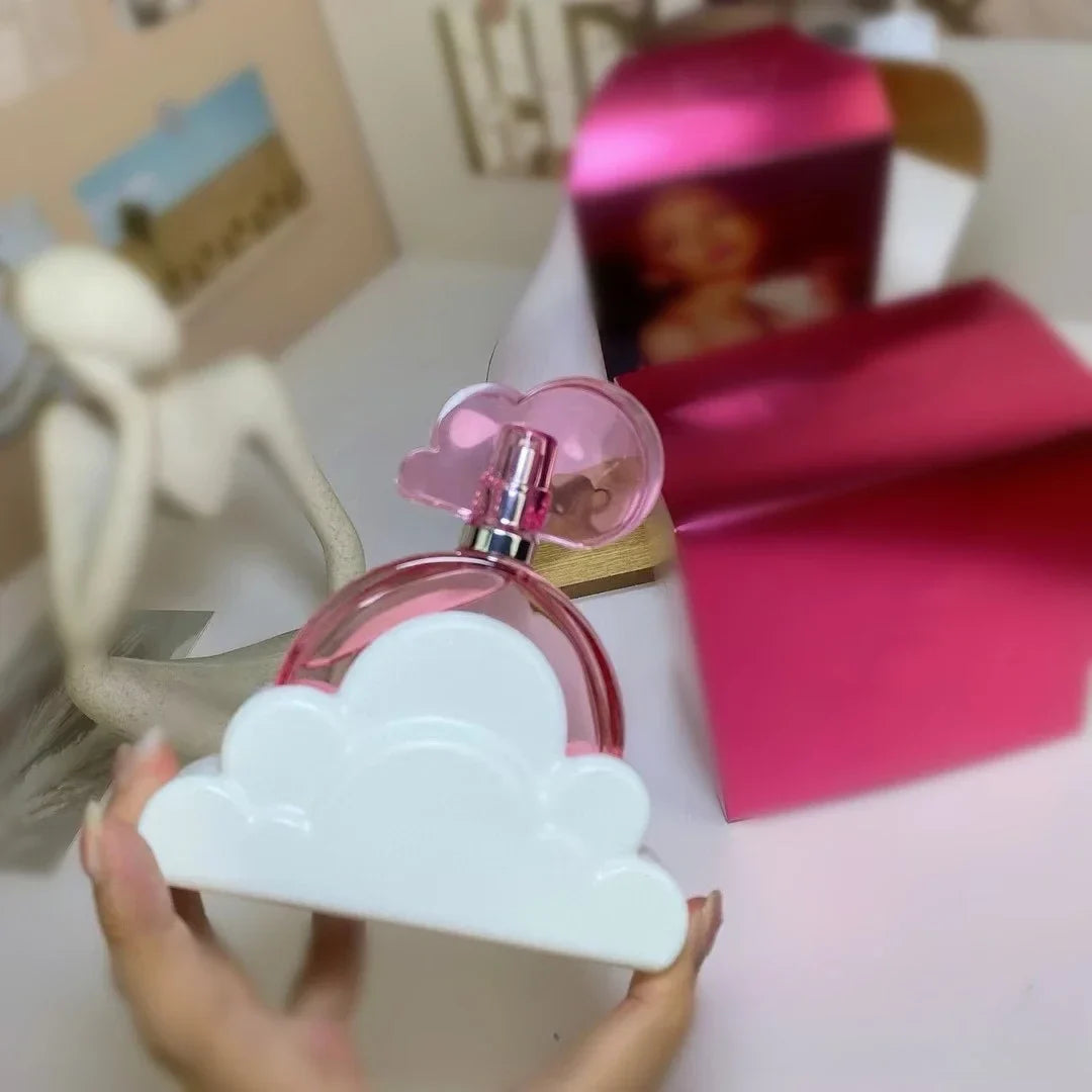 Pink and white cloud-shaped perfume bottle held by a hand on a blurred background