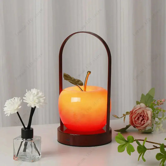 Decorative apple-shaped lamp with a wooden handle on a table with flowers and a diffuser.