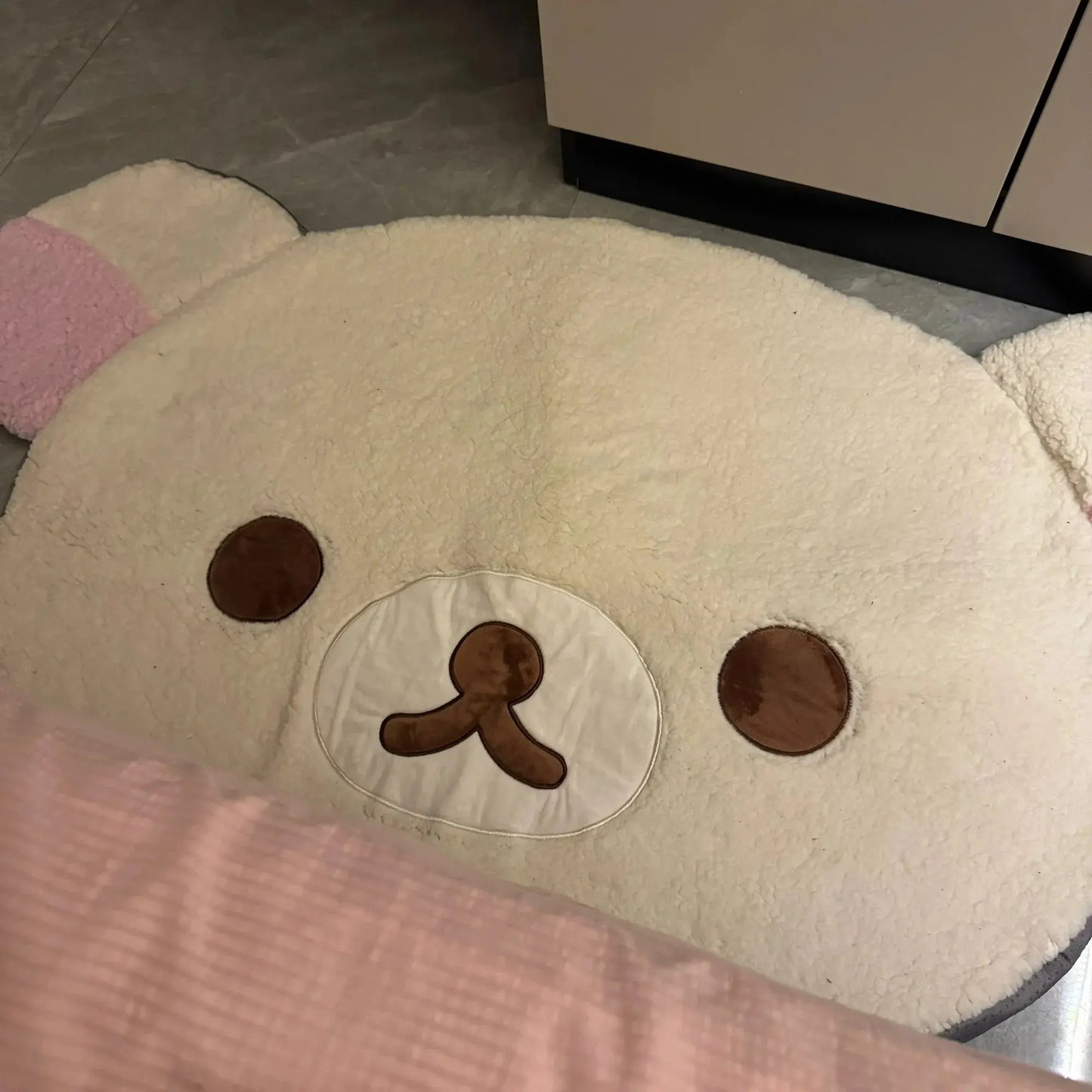 Cushion shaped like a bear face with brown eyes and nose on a light background