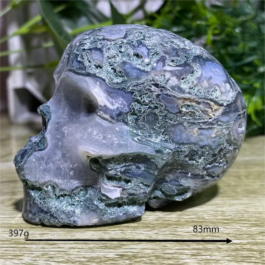 Decorative stone sculpture of a face on a wooden surface with greenery in the background