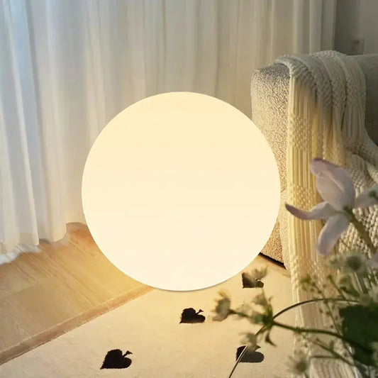 Large spherical lamp emitting a soft glow in a room with curtains and flowers.