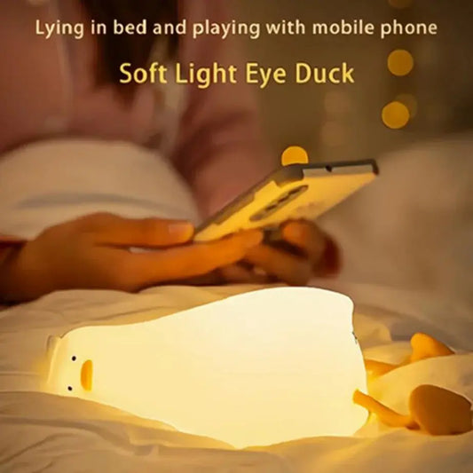 Person lying in bed using a smartphone with a soft light eye duck lamp nearby.
