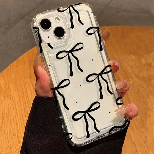 Phone case with black bow designs held by a hand on a wooden surface