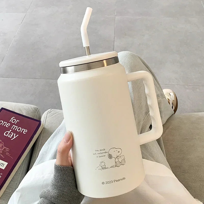Snoopy White mug with handle and straw lid held by a person, with a book titled 'For One More Day' on a couch.