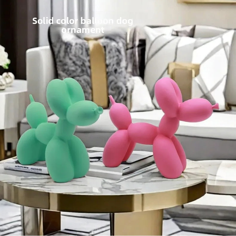 Two balloon dog ornaments, one green and one pink, on a marble table in a living room setting.