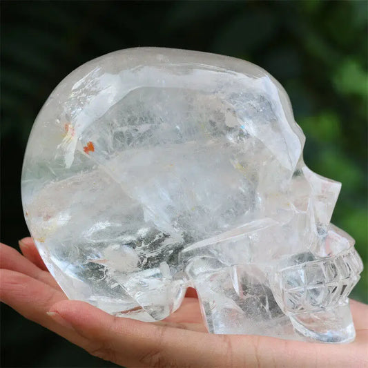 Clear crystal skull held in a hand with a blurred green background