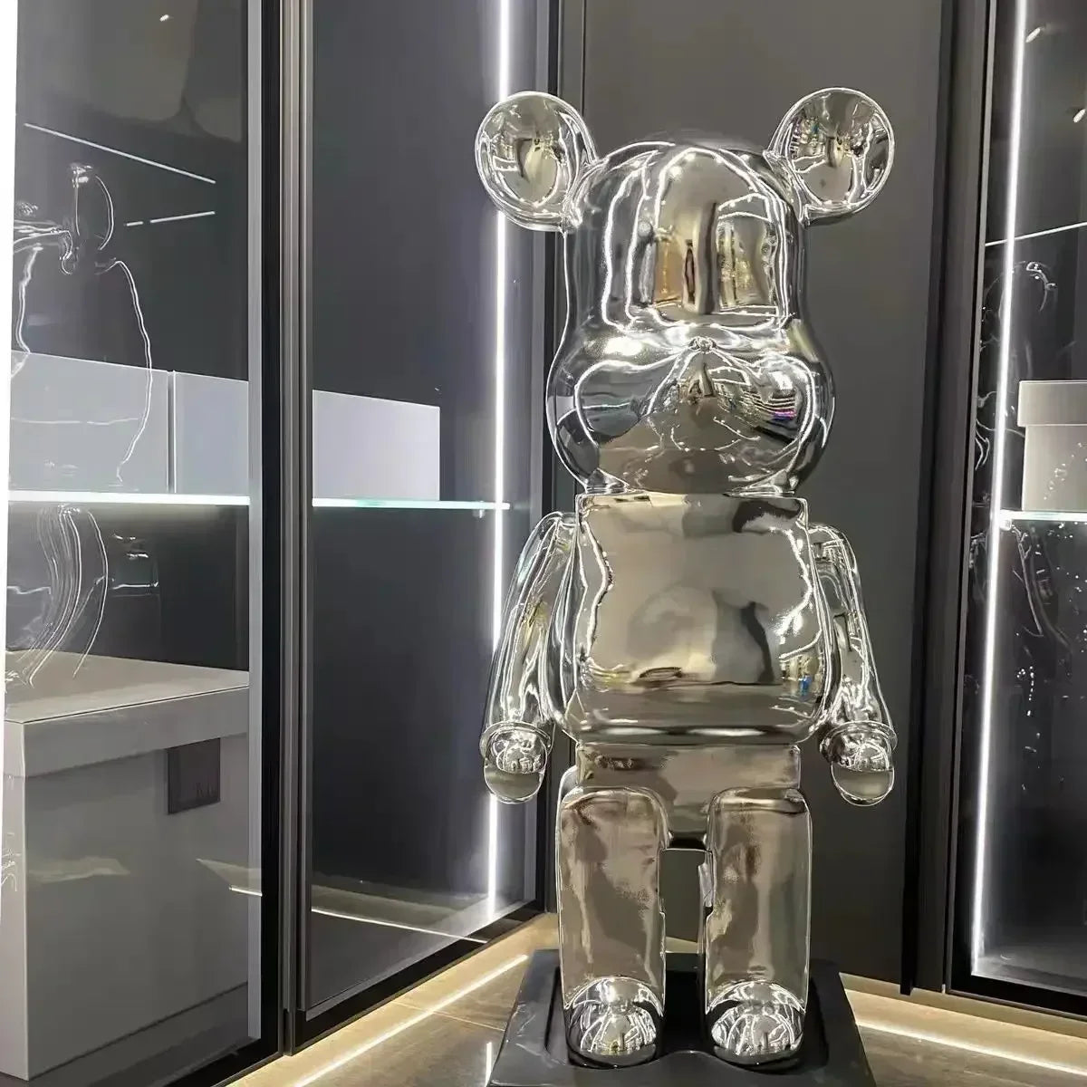 Silver bear-like figure with large round ears on a black stand against a dark background. bearbrick collectable