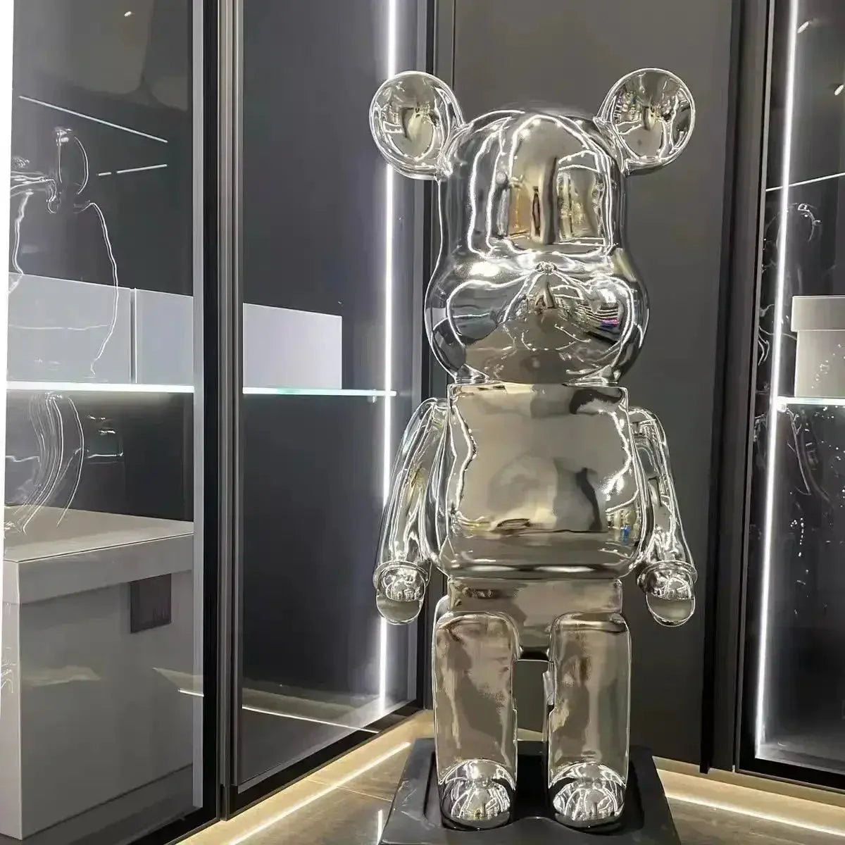 Silver bear-like figure with large round ears on a black stand against a dark background. bearbrick collectable