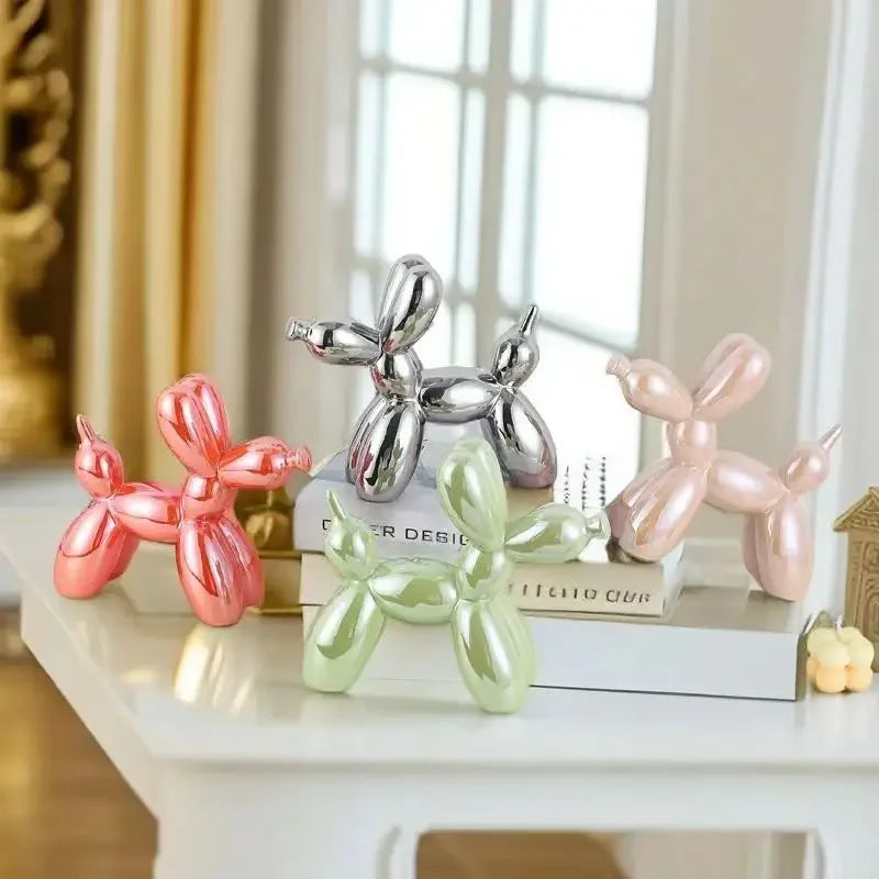 Four balloon dog sculptures in pink, green, silver, and pink on a shelf.