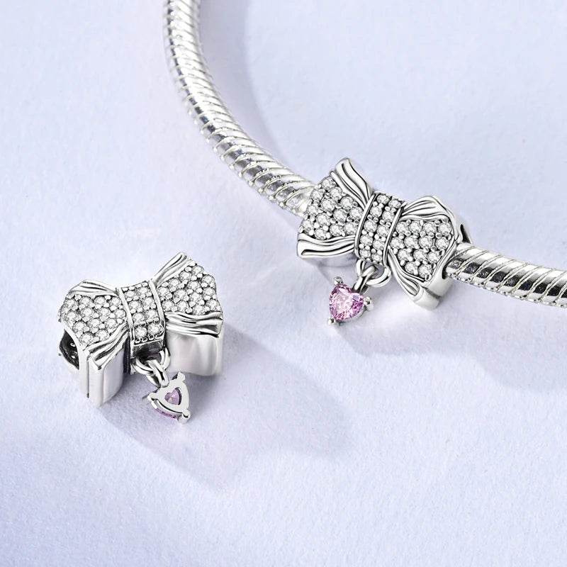 Silver bow-shaped charms with pink heart details on a white background. pandora style