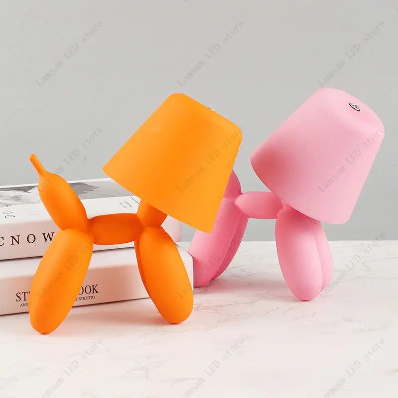 Orange and pink balloon dog toys on a light surface with books in the background.