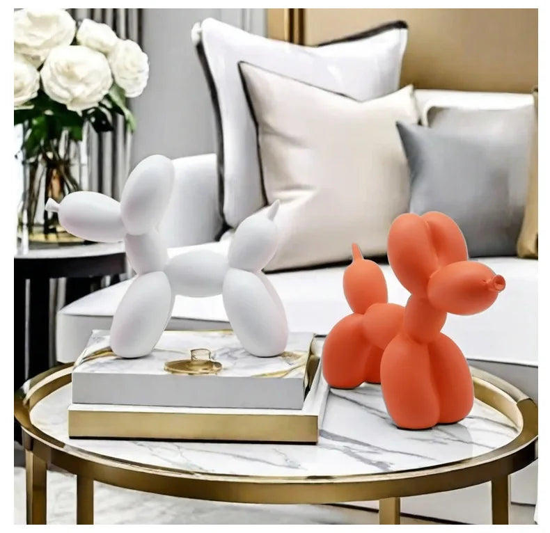 Two balloon dog sculptures, one white and one orange, on a marble coffee table with a modern living room background.