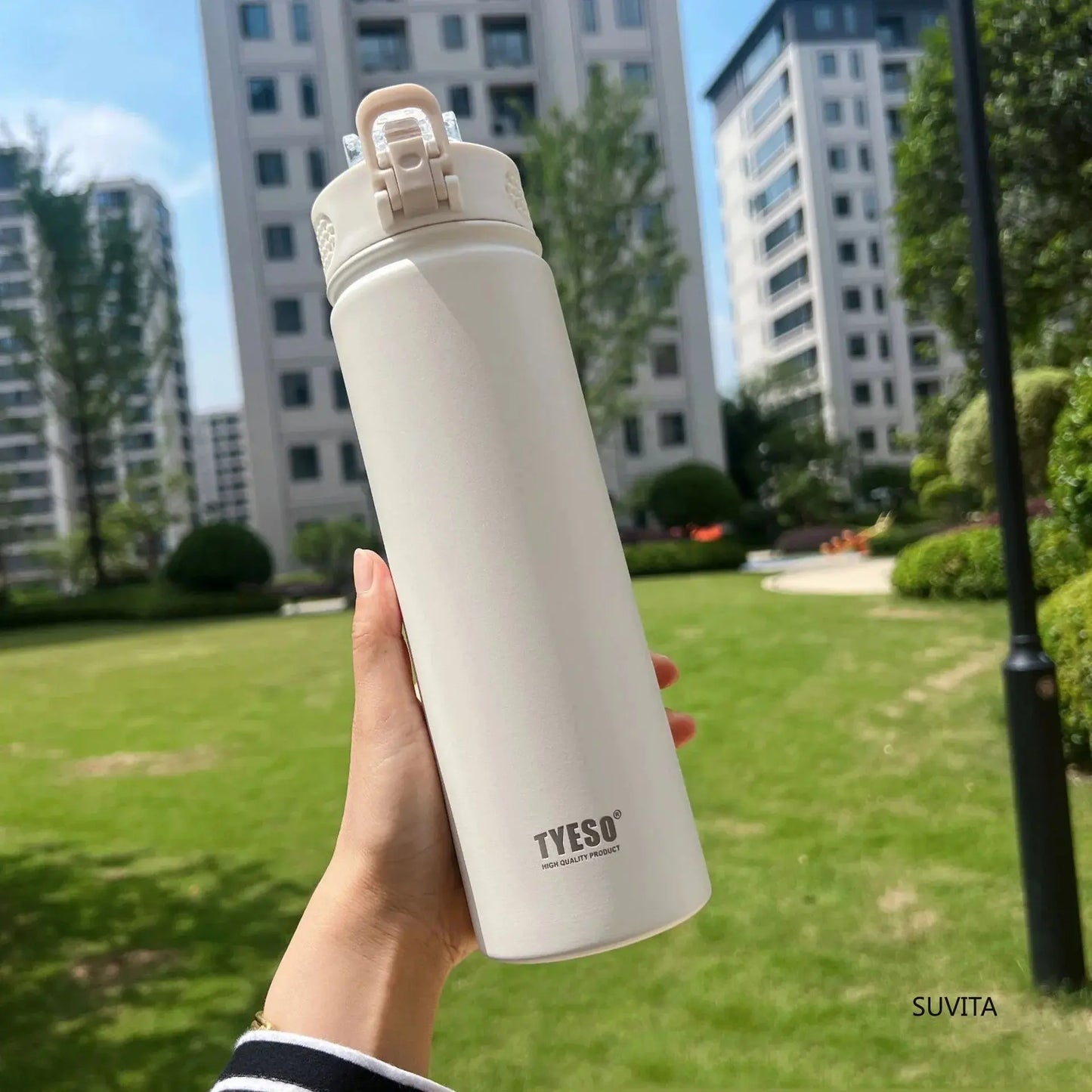 Hand holding TYESO white thermos bottle outdoors. BPA-free and insulated to keep drinks hot or cold for hours.