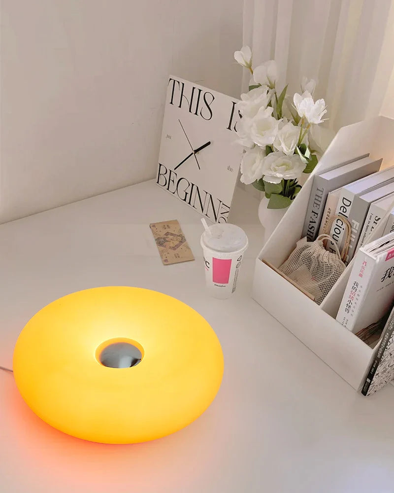 Yellow lamp on a desk with books, a cup, and flowers in the background
