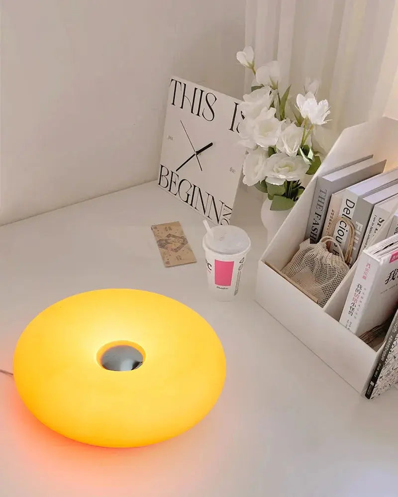 Yellow lamp on a desk with books, a cup, and flowers in the background