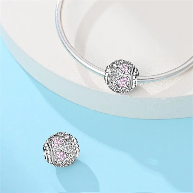 Silver charm with pink heart details on a light blue background. pandora style