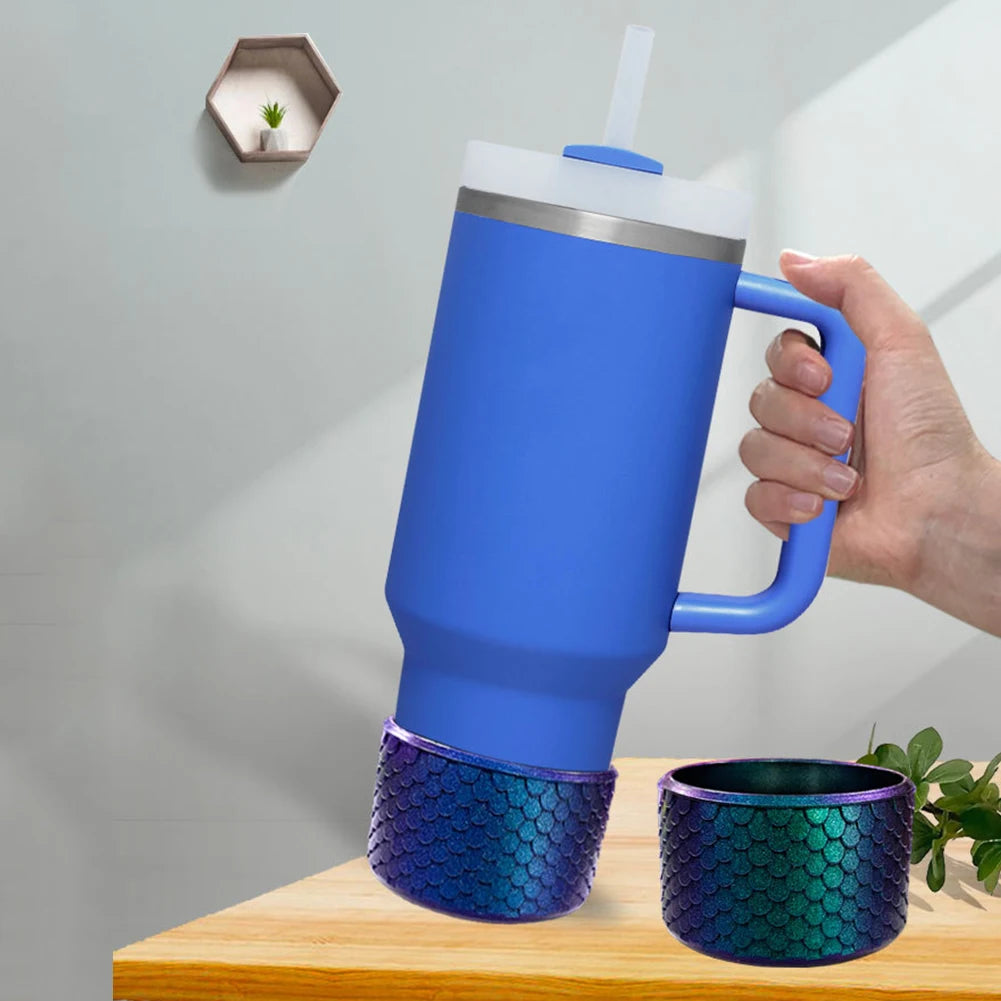 Stanley Blue insulated mug with handle held by a hand, with smaller blue and purple mermaid-scale mug below on a wooden surface.