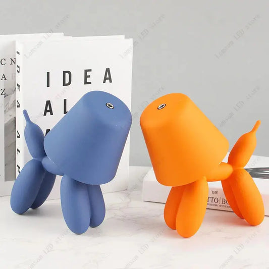 Blue and orange balloon dog figurines on a light surface with a book in the background.
