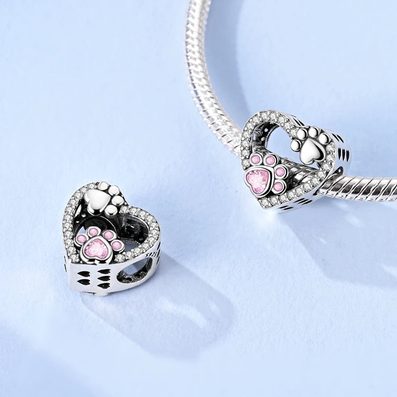 Heart-shaped paw print charm with pink gemstones on a light blue background. pandora style