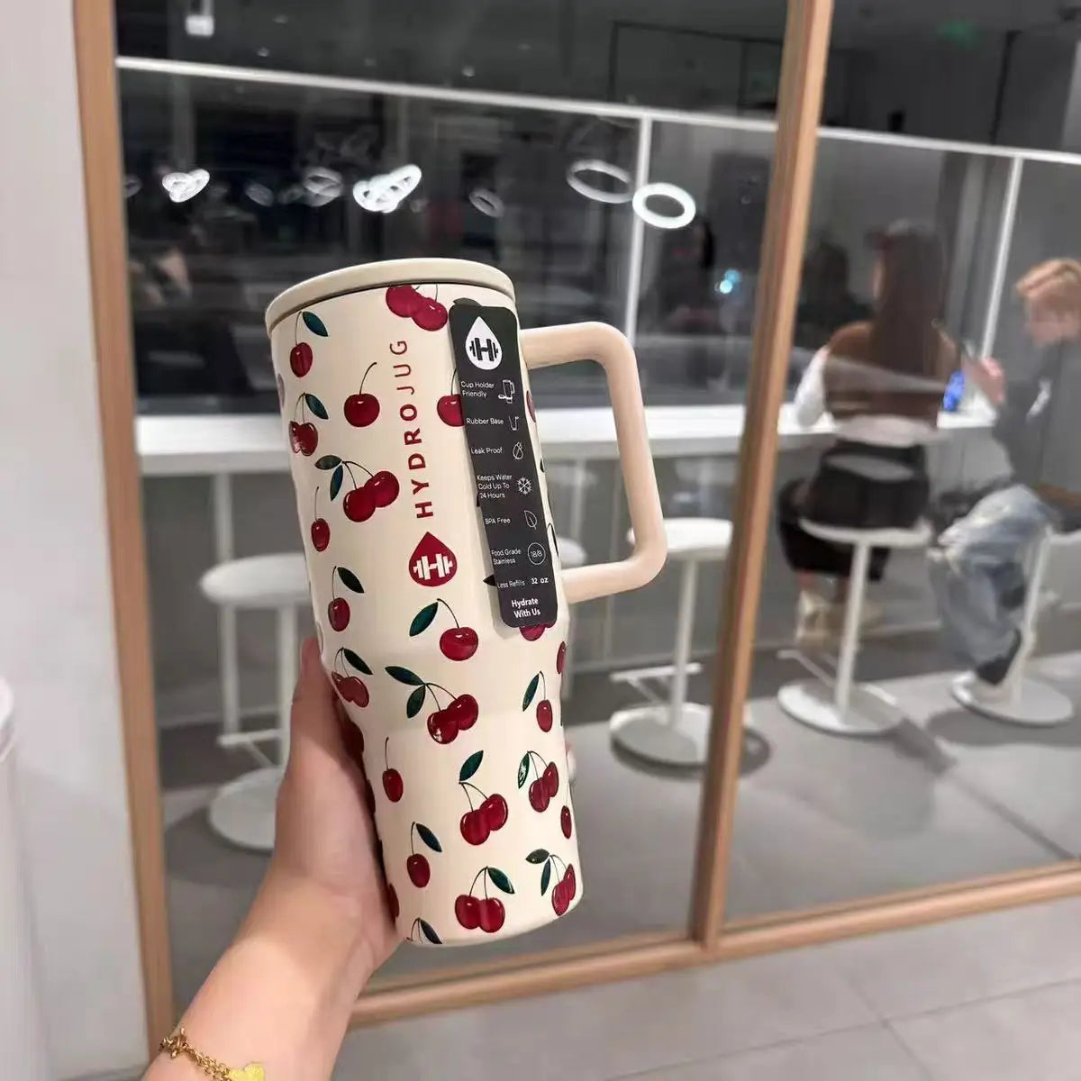 Cherry print HydroJug Gobelet 40OZ Voyageur Thermos held in hand, showcasing its fun design and practical features.
