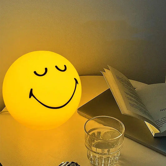 Smiley face night light on a table with a glass of water and an open book.