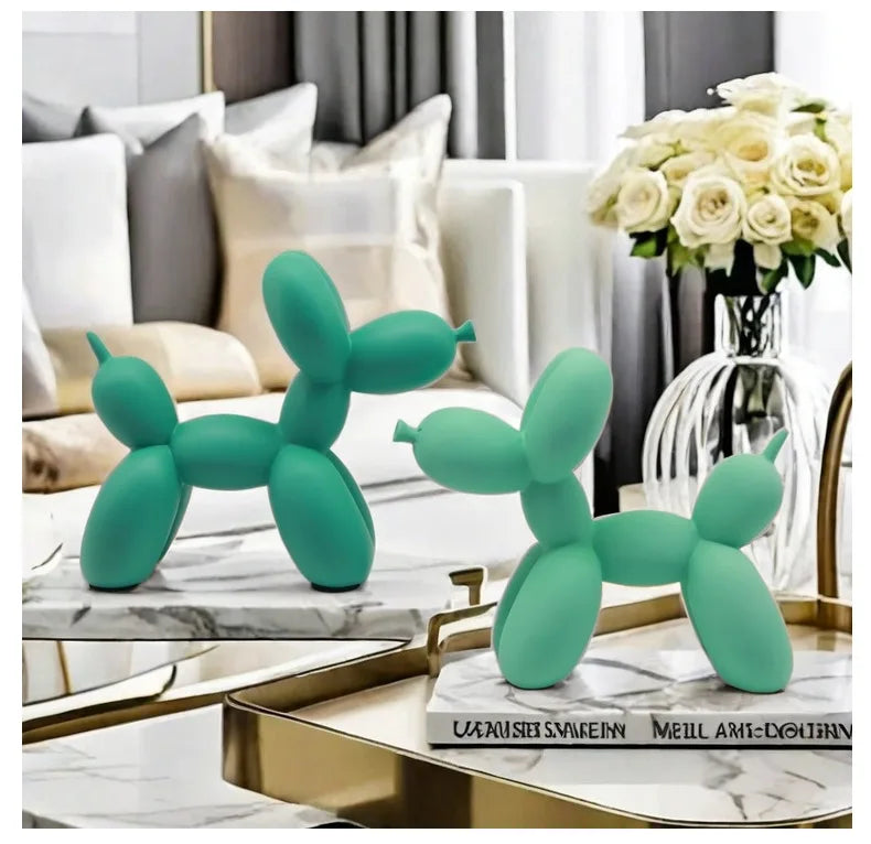 Two green balloon dog sculptures on a marble surface with a vase of flowers in the background.