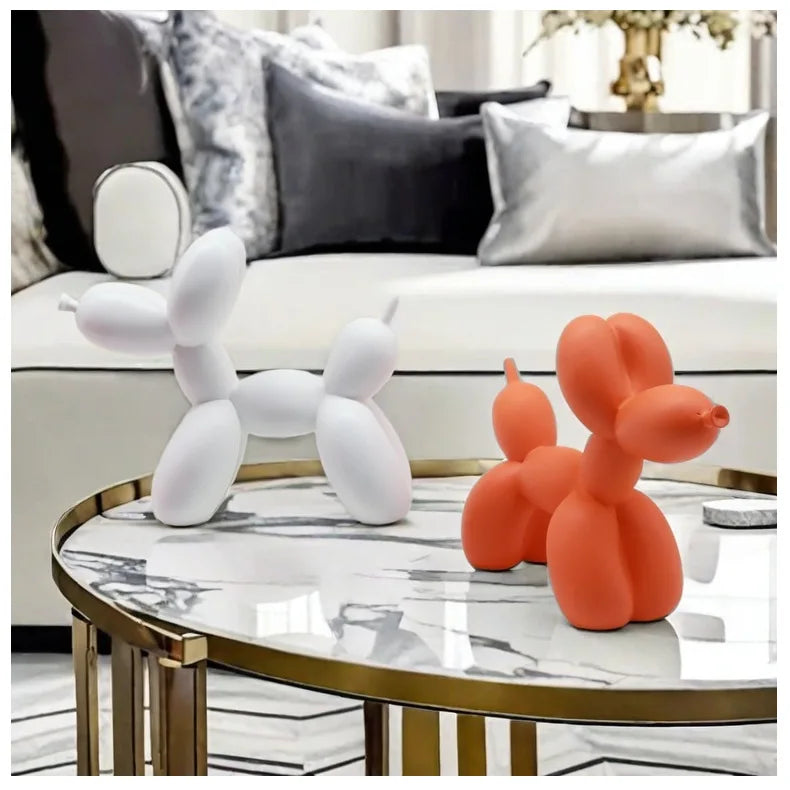 Two balloon dog sculptures, one white and one orange, on a marble coffee table with a living room background.