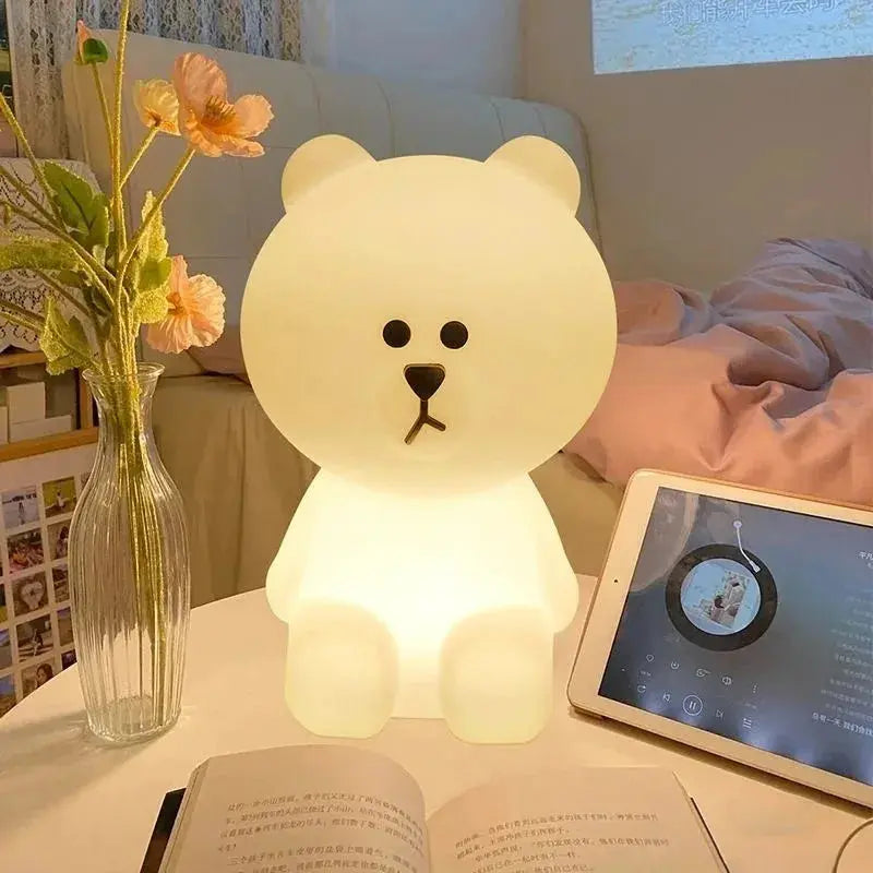 Bear-shaped night light on a table with a tablet and vase in a cozy room setting.