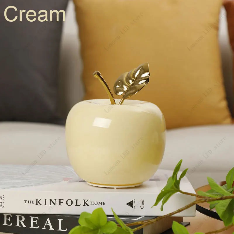 Decorative cream-colored apple with gold leaves on top of books, with 'The Kinfolk Home' visible.