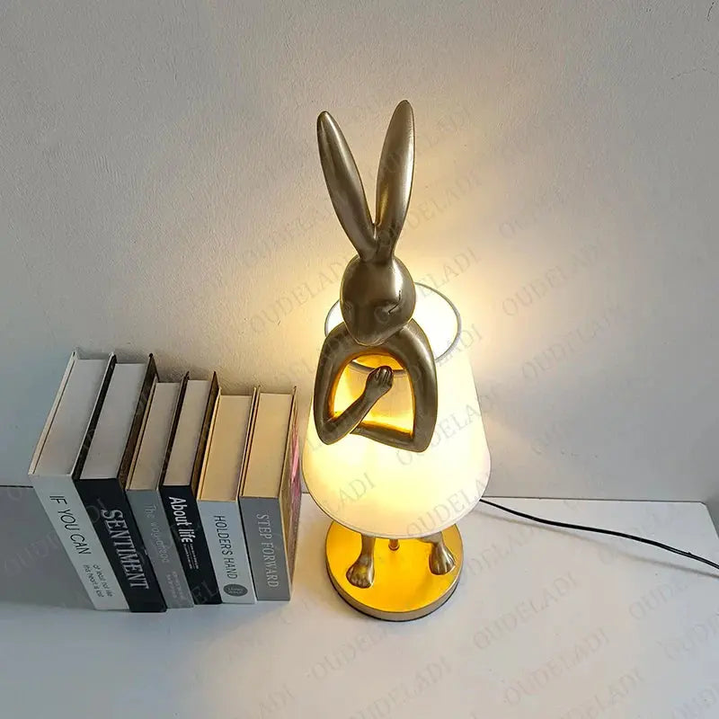 Decorative lamp shaped like a rabbit with a warm glow, placed on a surface with books.