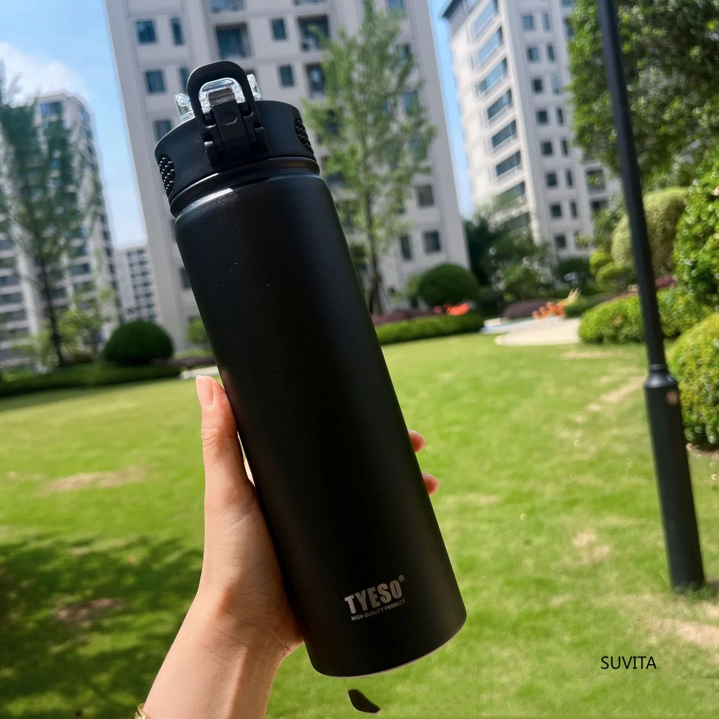 TYESO black thermos bottle with straw held in a green park. Leak-proof and BPA-free for daily hydration.