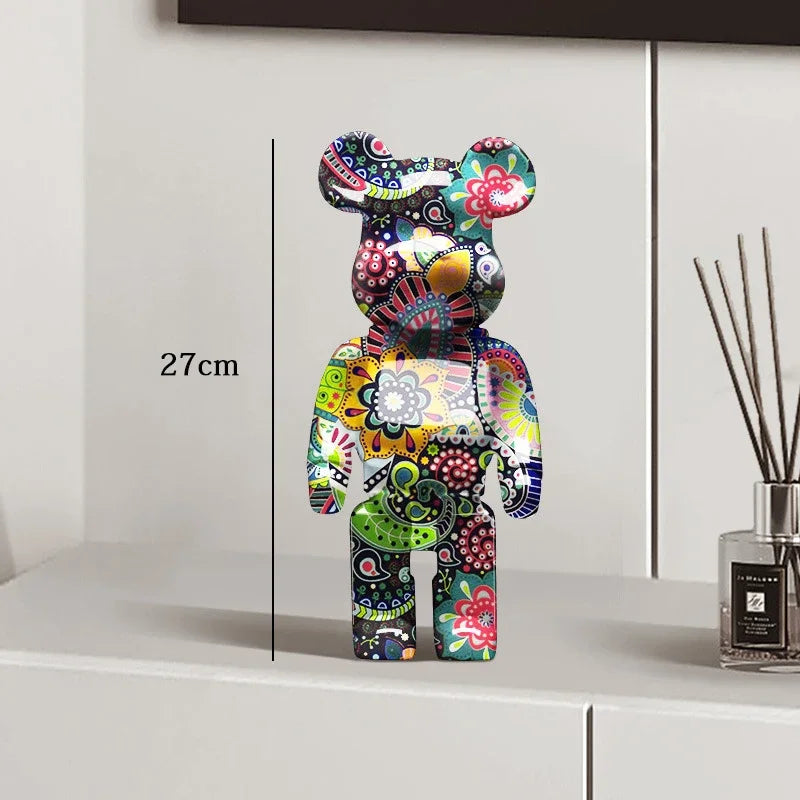 Colorful decorative bear figure on a white surface with a vase in the background be@rbrick collectable