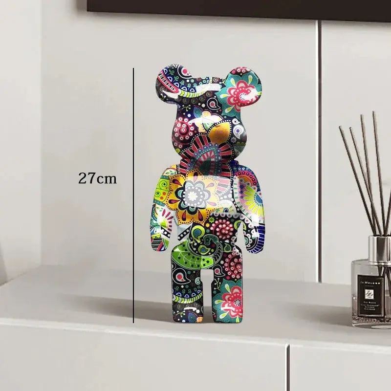 Colorful decorative bear figure on a white surface with a vase in the background be@rbrick collectable