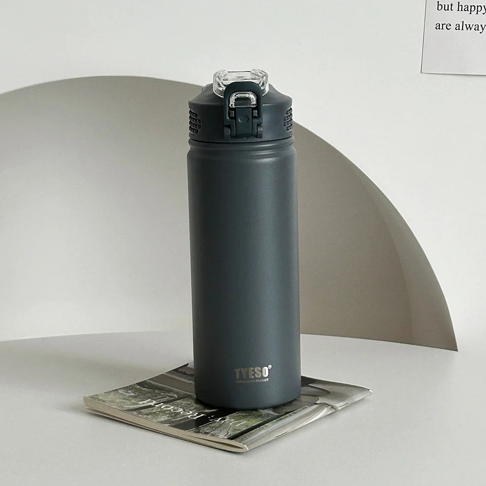 TYESO gray thermos bottle with straw on a magazine. Leak-proof and BPA-free, ideal for home or office use.