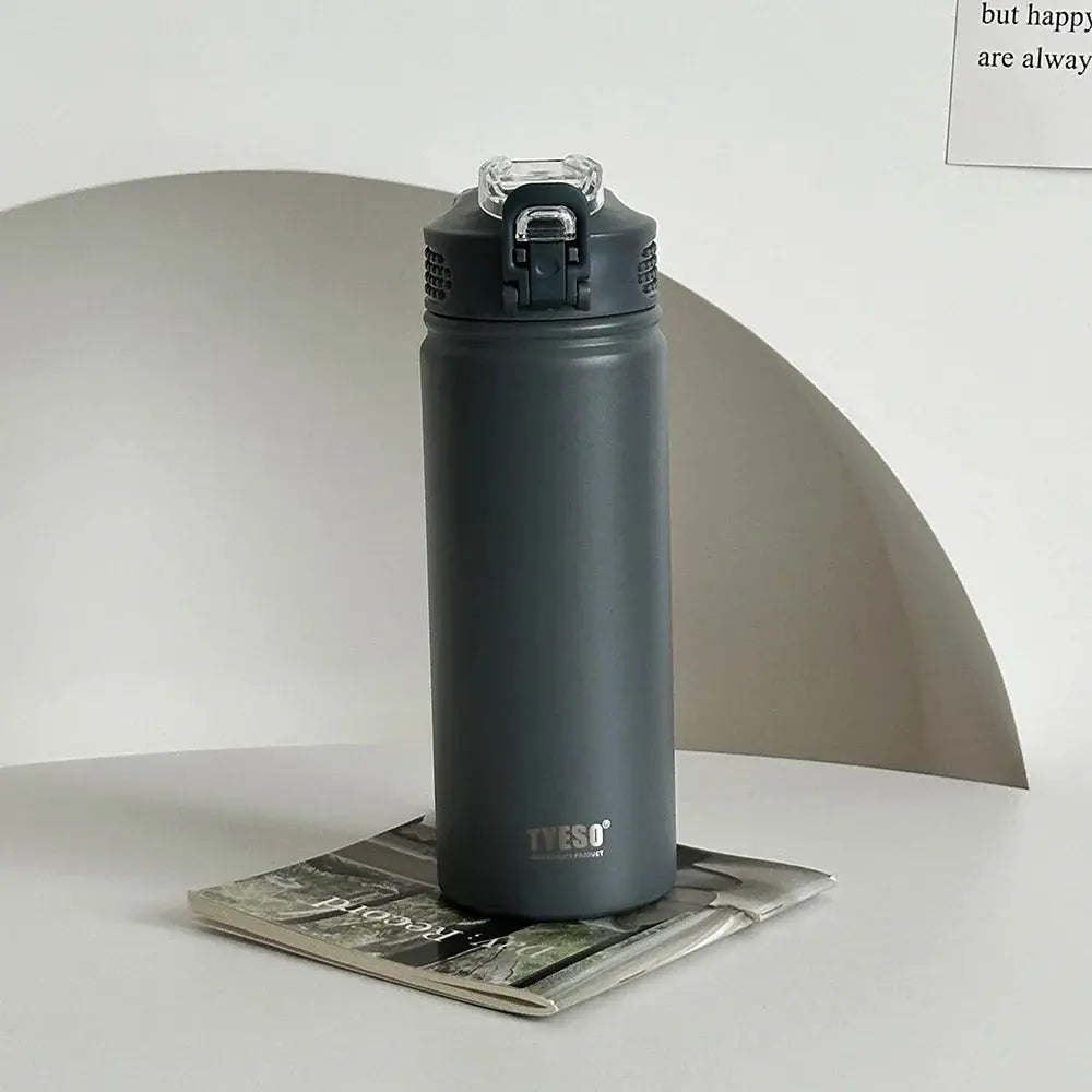 TYESO gray thermos bottle with straw on a magazine. Leak-proof and BPA-free, ideal for home or office use.