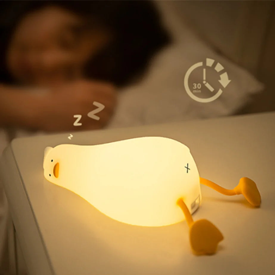 Glowing night light shaped like a cartoon character on a bedside table with a person lying in bed in the background.