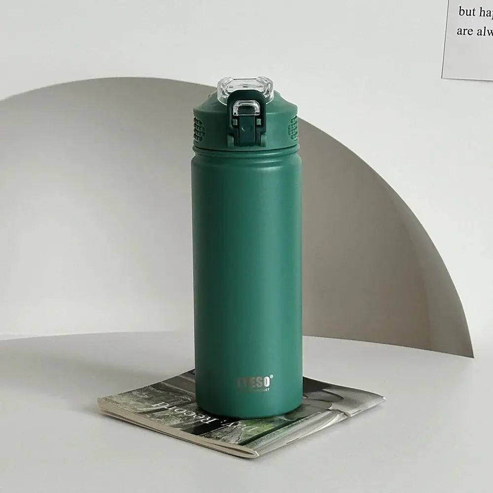 TYESO green thermos bottle with straw on a magazine. Double-wall insulated and BPA-free for hot or cold drinks.