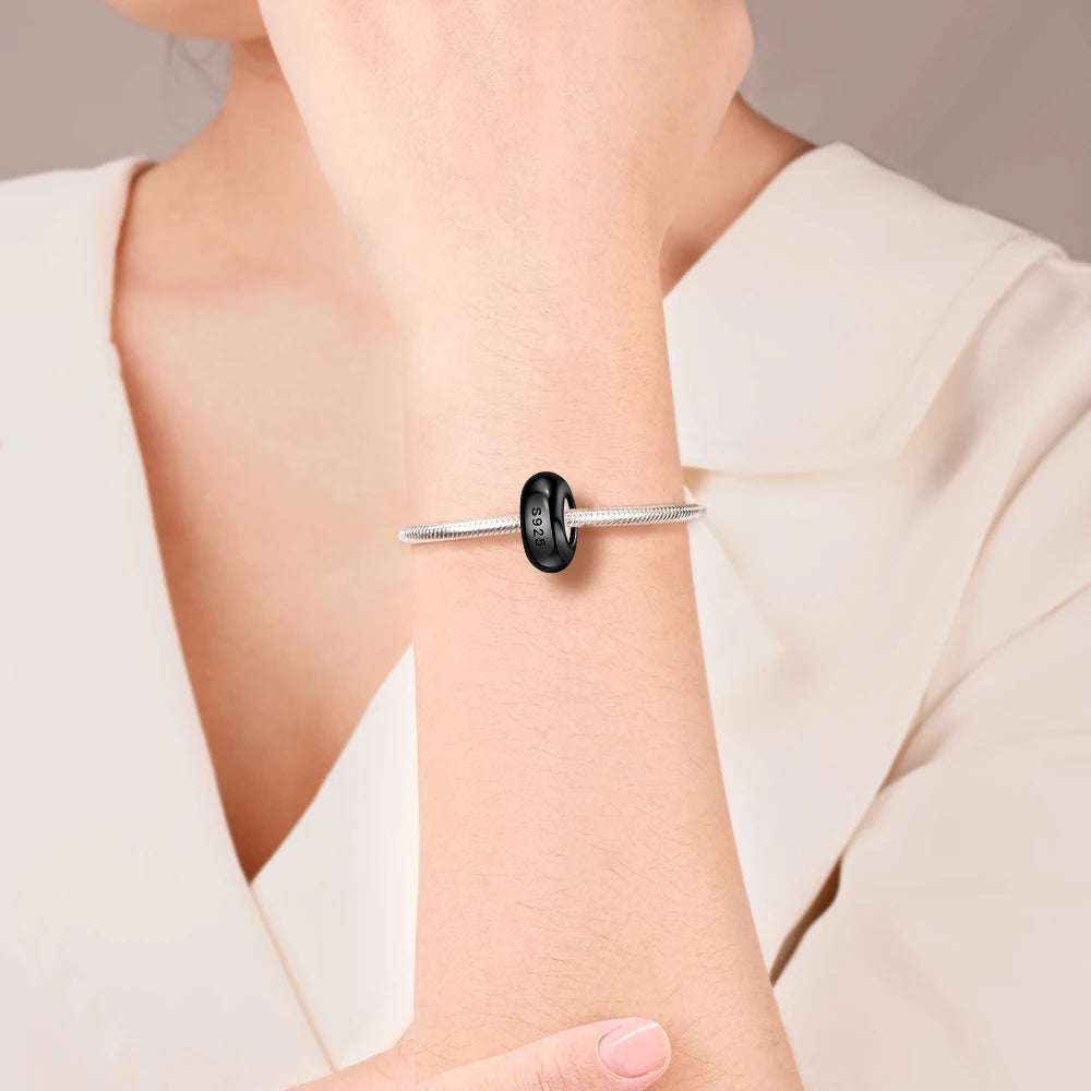 Silver bracelet with a black bead on a person's wrist against a neutral background pandora style charm pendant
