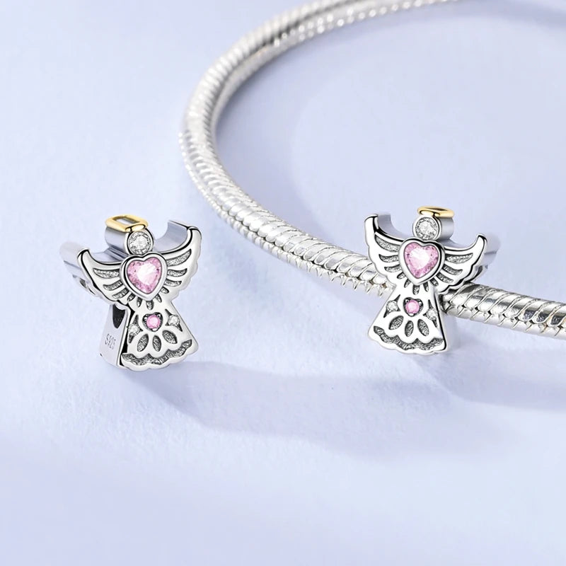 Two angel-shaped charms with pink hearts on a light purple background. pandora style