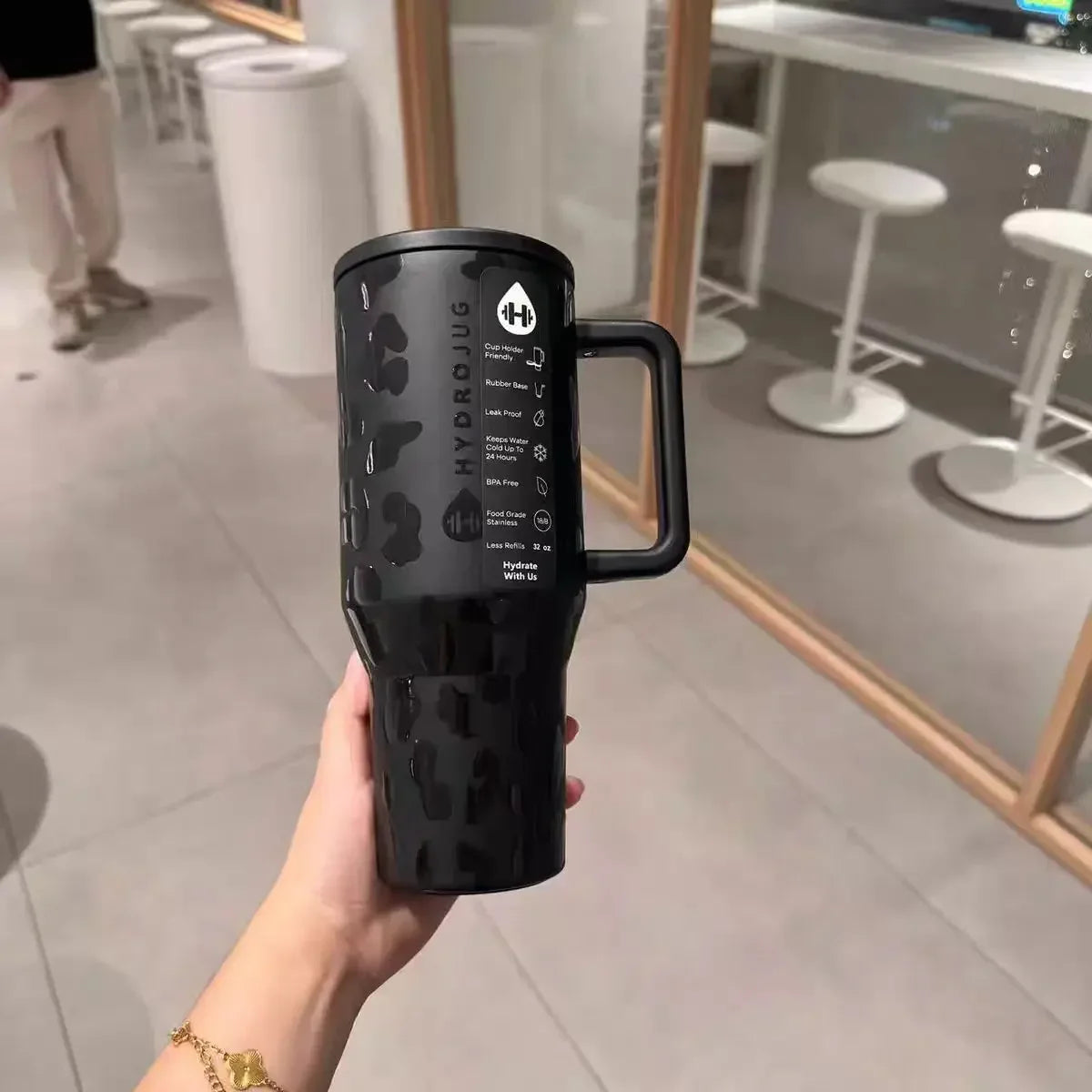 Hand holding black leopard HydroJug Gobelet 40OZ Voyageur Thermos in a modern setting, highlighting its sleek and practical design.
