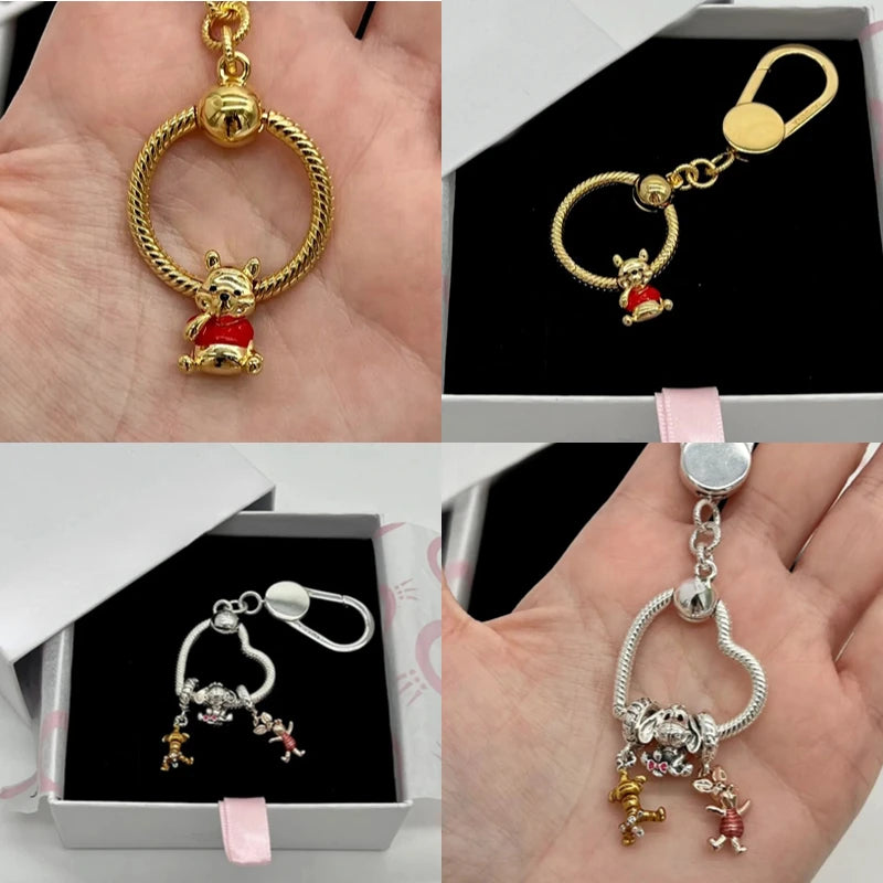 Gold and silver keychains with bear charms displayed in hands and a box. Disney